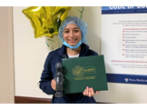 Abheena Jacob holds a Daisy Award and certificate in front of balloons in a Pennsylvania Hospital hallway.